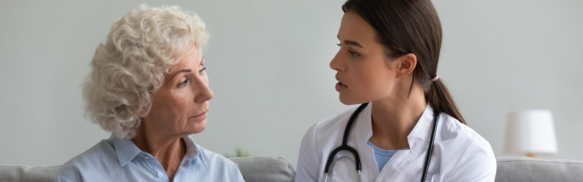 Young woman doctor visit sick senior grandmother at home consult about prescribed medicine